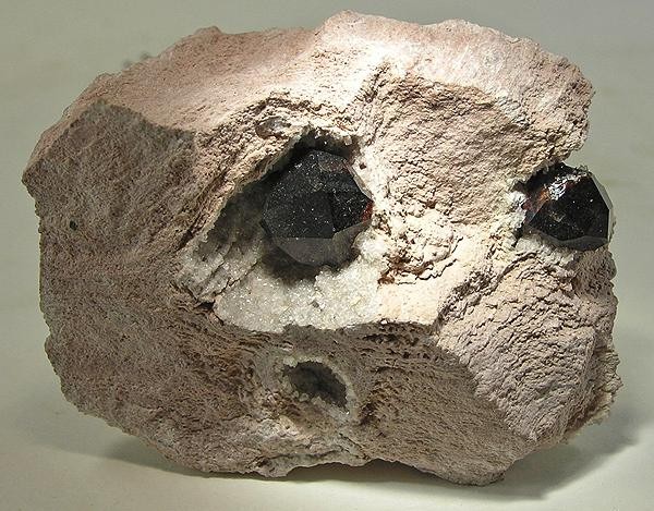 Twin dark red Almandine garnet crystals exposed inside weathered volcanic matrix